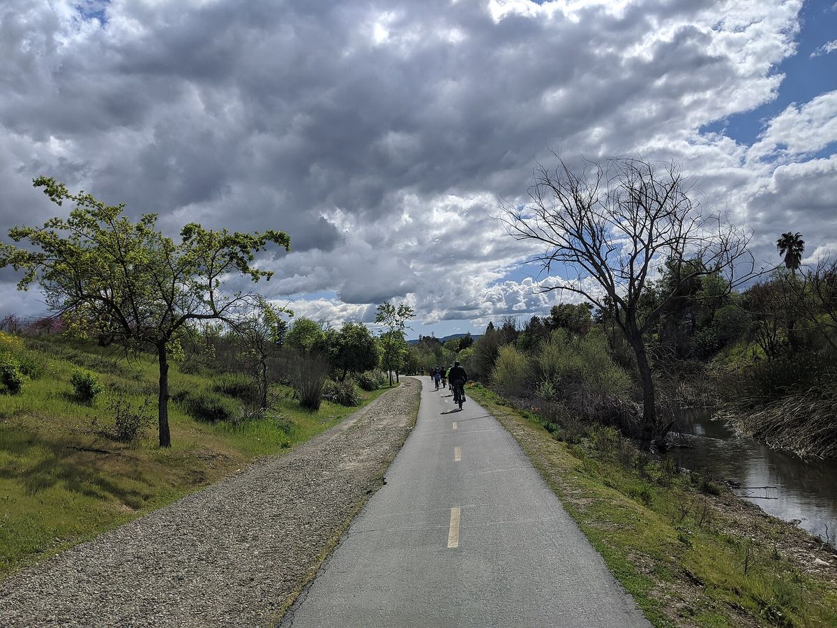 A cyclist on the Los Gatos Creek Trail under a cloudy sky
